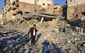 A man makes his way through debris at the site of an Israeli airstrike that targeted the offices of Al-Qard al-Hassan, a Hezbollah-linked financial institution, in the southern coastal Lebanese city of Tyre on March 2, 2026. Israel bombarded Lebanon on March 2, expanding the conflict across the region after the massive Israel-US attack on Iran that the US president launched to topple Tehran's ruling clerics, and killing their supreme leader o February 28. (Photo by KAWNAT HAJU / AFP)