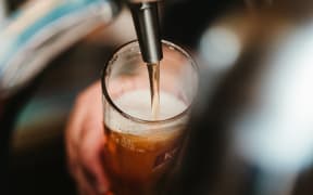 A person's hand can be seen holding a beer glass as the beer pours from a tap in a bar.