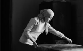 This is a black and white image of a young woman ironing silk at the Yodgorlik Silk Factory