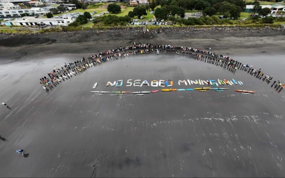 Surfboards and water craft spelled-out ‘no seabed mining’ on the black sand of Autere.