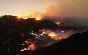 Flames and smoke from the Palisades Fire surround a home (C) in the community of Topanga, California, on January 9, 2025. The two largest fires burning in Los Angeles remain "zero percent" contained on January 9 despite firefighting operations, officials said, as they also vowed to tackle looting of evacuated homes. A 17,000-acre (6,900-hectare) blaze in Pacific Palisades has become "one of the most destructive natural disasters in the history of Los Angeles," said city fire chief Kristin Crowley, while a 10,000-acre fire in Altadena was also at "zero percent containment," said county fire chief Anthony Marrone. (Photo by David Swanson / AFP)