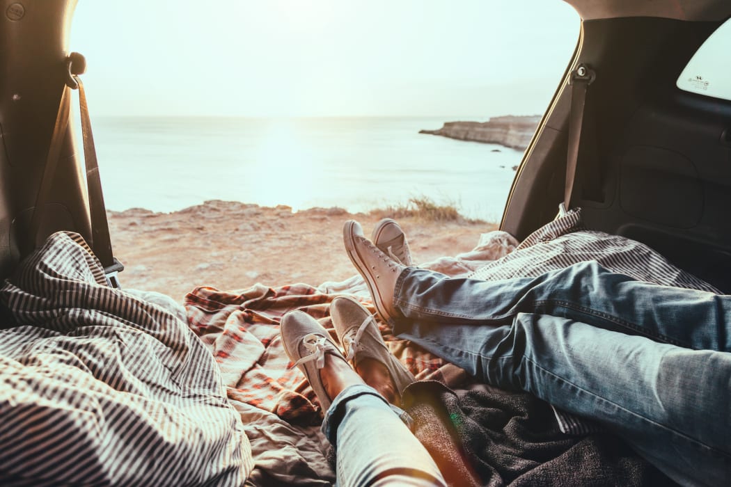 Man and woman relaxing inside trunk and watching at the sea. Fall car trip in sunset. Freedom travel concept. weekend.