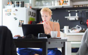 Female freelancer in her casual home clothing working remotly from her dining table in the morning. Home kitchen in the background.