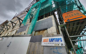 The side of the multi-storey half-finished building covered by scaffolding and netting.