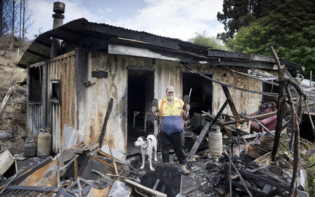 Palmerston man Kevin Lott and his dog, Patch, stand in the remnants of his off-grid container home that went up in flames last week. PHOTO: GERARD O’BRIEN