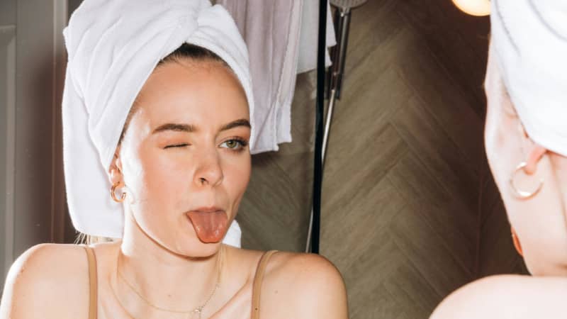 A woman pokes her tongue out in the bathroom window