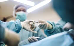 Surgeons in sterile gowns and gloves pass a scalpel, demonstrating teamwork and precision in surgery.