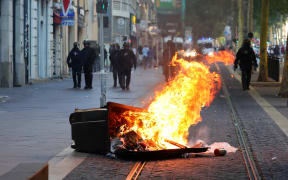French riot police officers stand guard behind a burnt trash bin during a demonstration against police in Marseille, southern France on July 1, 2023, after a fourth consecutive night of rioting in France over the killing of a teenager by police. French police arrested 1311 people nationwide during a fourth consecutive night of rioting over the killing of a teenager by police, the interior ministry said on July 1, 2023. France had deployed 45,000 officers overnight backed by light armoured vehicles and crack police units to quell the violence over the death of 17-year-old Nahel, killed during a traffic stop in a Paris suburb on July 27, 2023. (Photo by CLEMENT MAHOUDEAU / AFP)