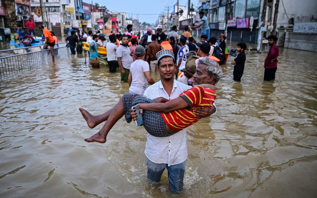 A youth carries an elderly man as they wade through a flooded street after heavy rainfall in Wellampitiya on the outskirts of Colombo on November 30, 2025.
