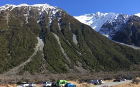 Blue skies and snow capped mountain with cars at base