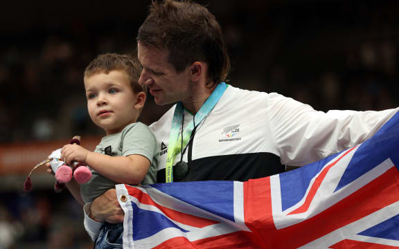 Gold medallist Aaron Gate holds son Axel as he celebrates during the medal presentation ceremony for the men's 1000m time trial cycling event at the Commonwealth Games on 1 August 2022.