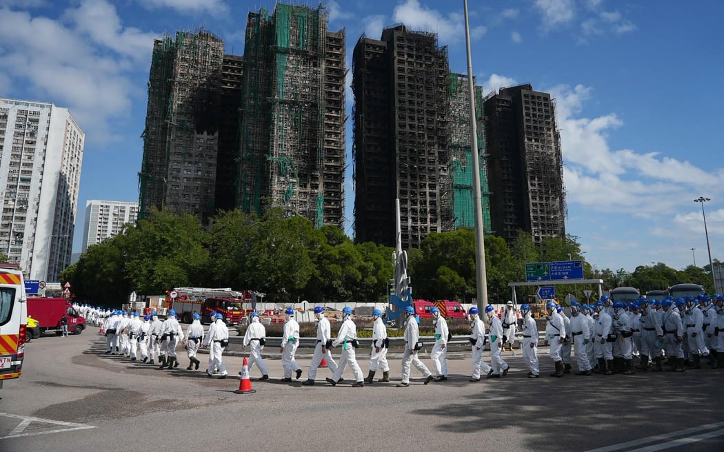 Police officers from the Disaster Victim Identification Unit (DVIU), dressed in white-coloured full-body protective gear, walk past the housing blocks of Wang Fuk Court in the aftermath of the deadly November 26 fire, in Hong Kong on November 29, 2025.  (Photo by Yan ZHAO / AFP)