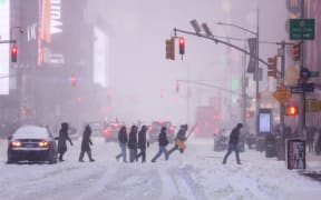 People walk across Sixth Avenue as snow falls in New York City on January 25, 2026. A massive winter storm on January 24 dumped snow and freezing rain from New Mexico to North Carolina as it swept across the United States towards the northeast, threatening tens of millions of Americans with blackouts, transportation chaos and bone-chilling cold. After battering the country's southwest and central areas, the storm system began to hit the heavily populated mid-Atlantic and northeastern states as a frigid air mass settled in across the nation. (Photo by CHARLY TRIBALLEAU / AFP)
