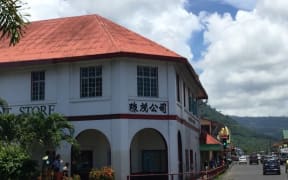 White 2 story Chinese supermarket in Apia, Samoa with terracotta tiled roof and Chinese signage. .