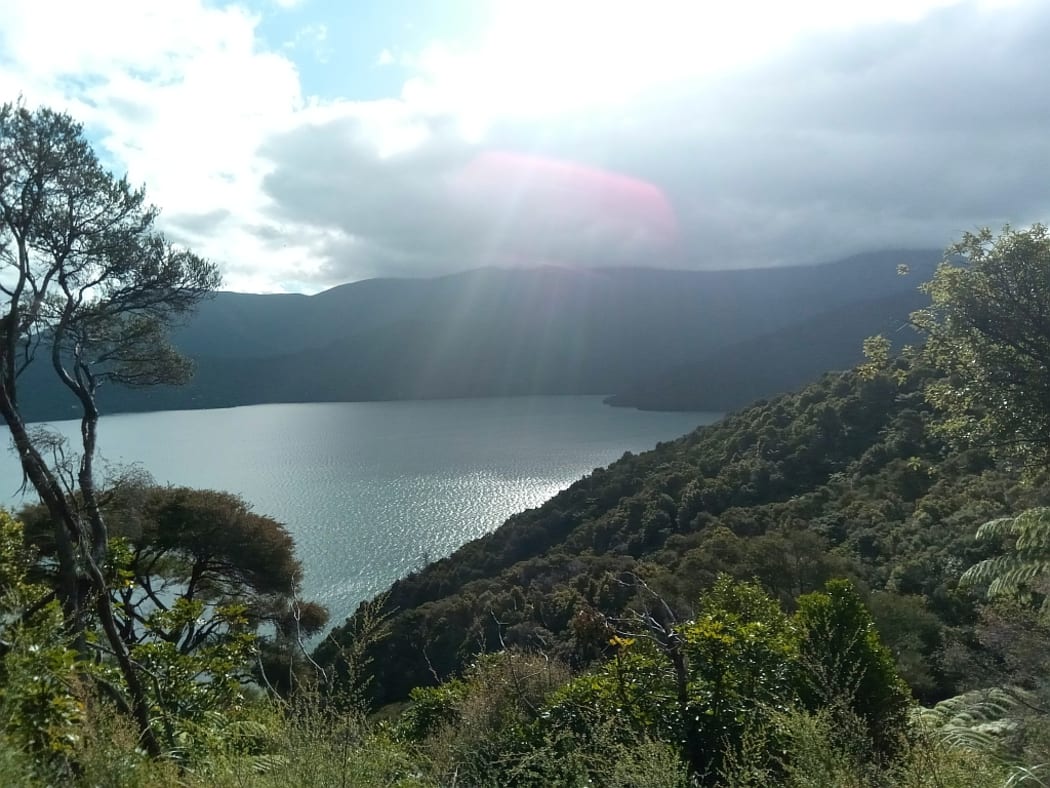 Sunshine breaking through clouds strikes reflects off the water in a bay.