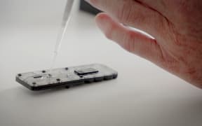 A close up of a hand using a pipette to drop clear liquid into a small plastic rectangular device.