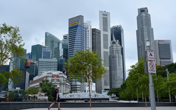A man walks through a park next to financial business district in Singapore on April 7, 2022. (Photo by Roslan RAHMAN / AFP)