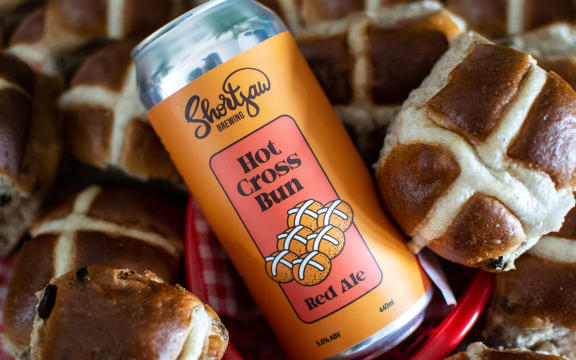 A can of Shortjaw Brewing Hot Cross Bun Red Ale lying amongst some hot cross buns