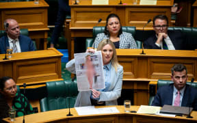 ACT MP Laura McClure holds up a faked nude photo of herself that she created when discussing the Deepfake Digital Harm and Exploitation Bill.