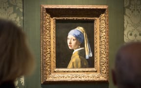 Visitors looks at the Johannes Vermeer's painting "Girl with a Pearl Earring" at the Mauritshuis museum in The Hague, 27 October 2022. - Dutch police arrested three people after climate activists targeted Johannes Vermeer's painting "Girl with a Pearl Earring".