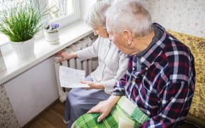 The senior woman holding gas bill in front of heating radiator. Payment for heating in winter.