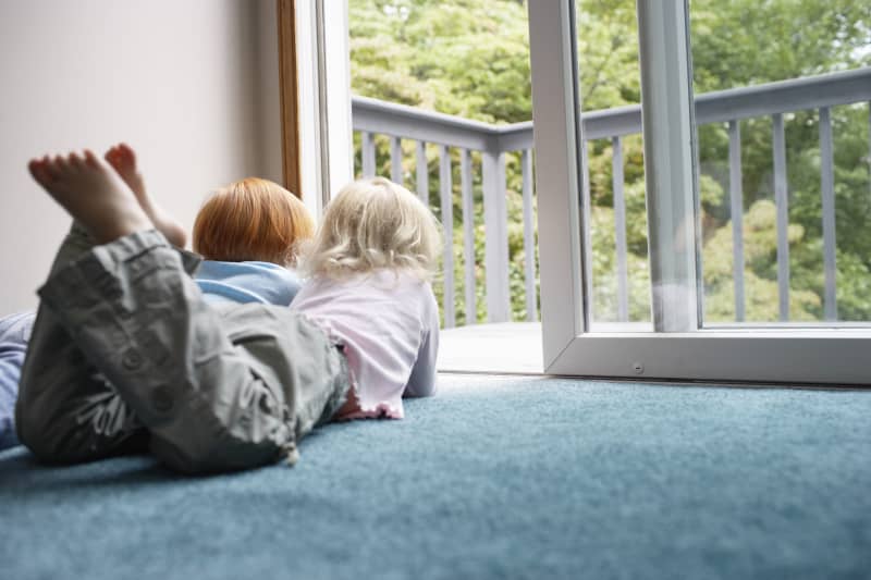 Sisters (3-6) lying on carpet looking through balcony door