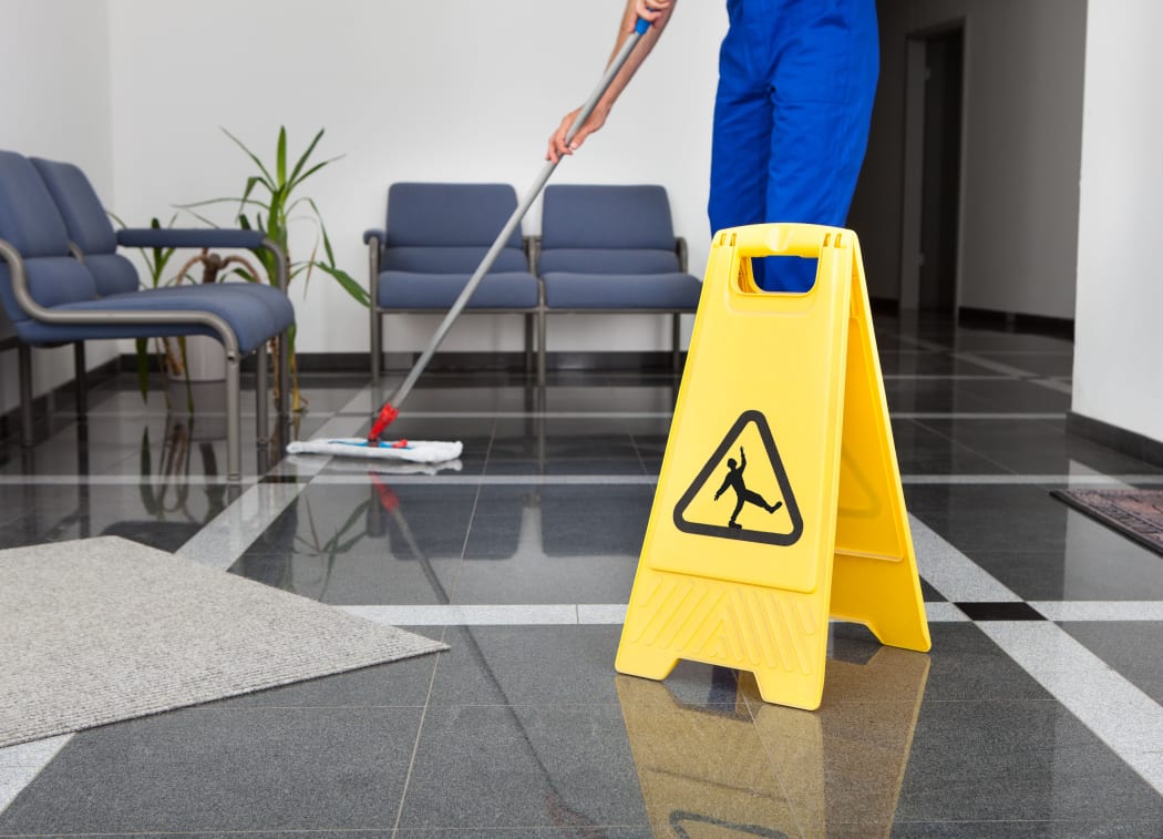 A worker mops a floor next to a 'cleaning in progress' sign.