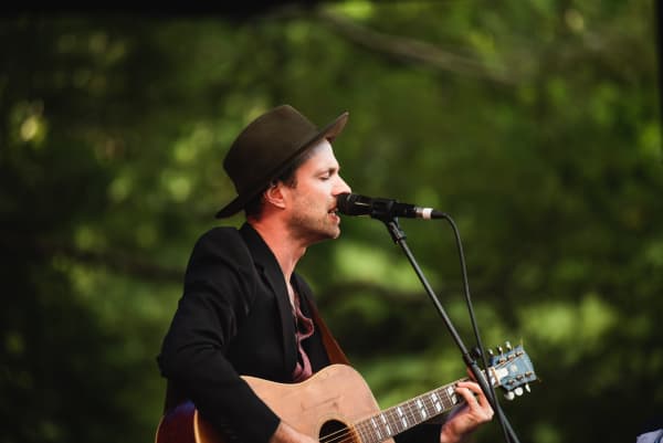 Finn Andrews of The Veils on stage at WOMAD, holding a guitar and wearing a black fedora style hat.