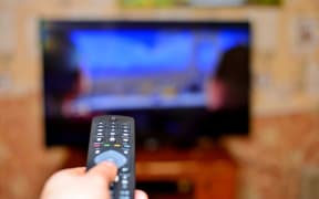 The man with the remote control in hand watching the sports channel and presses the button on the remote control. Remote control in hand closeup.