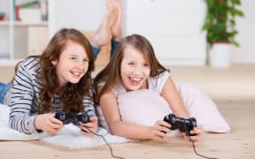 A photo of two young girls happily playing video games in a console laying on the living-room floor