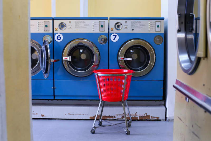 A red laundry trolley stands in front of a row of blue washing machines in a laundromat.