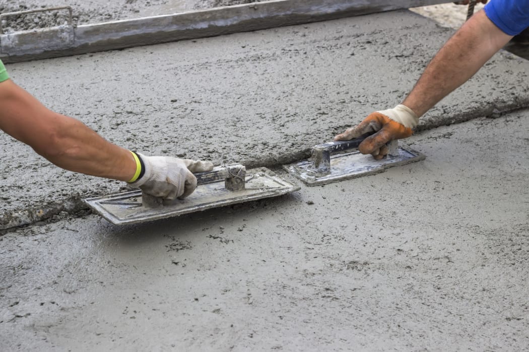 Leveling concrete with trowels, mason hands spreading poured concrete. Selective focus.
