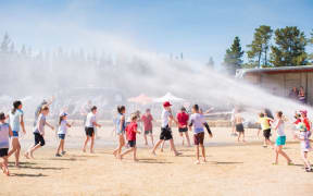 Children play underneath a sprinkler at a showground.
