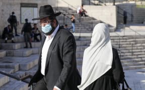 A Palestinian woman and a religious Jewish man walk past each other at the Damascus Gate of the old city of Jerusalem, on May 31, 2020.