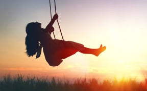 Happy laughing child girl on swing in sunset summer.