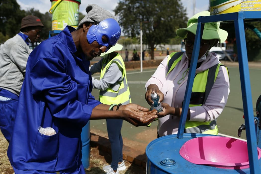 A health professional sprays disinfectant on a homeless man's hands before he queues to drink Methadone Oral Solution, provided as an effort to care for drug dependent people, at a shelter at the Lyttelton Sports Centre in Pretoria on April 16, 2020