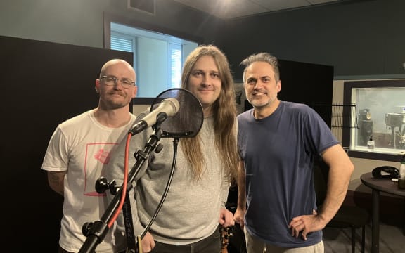 The band Tom Lark stand behind a microphone in the RNZ Wellington studio. They are a three piece band.