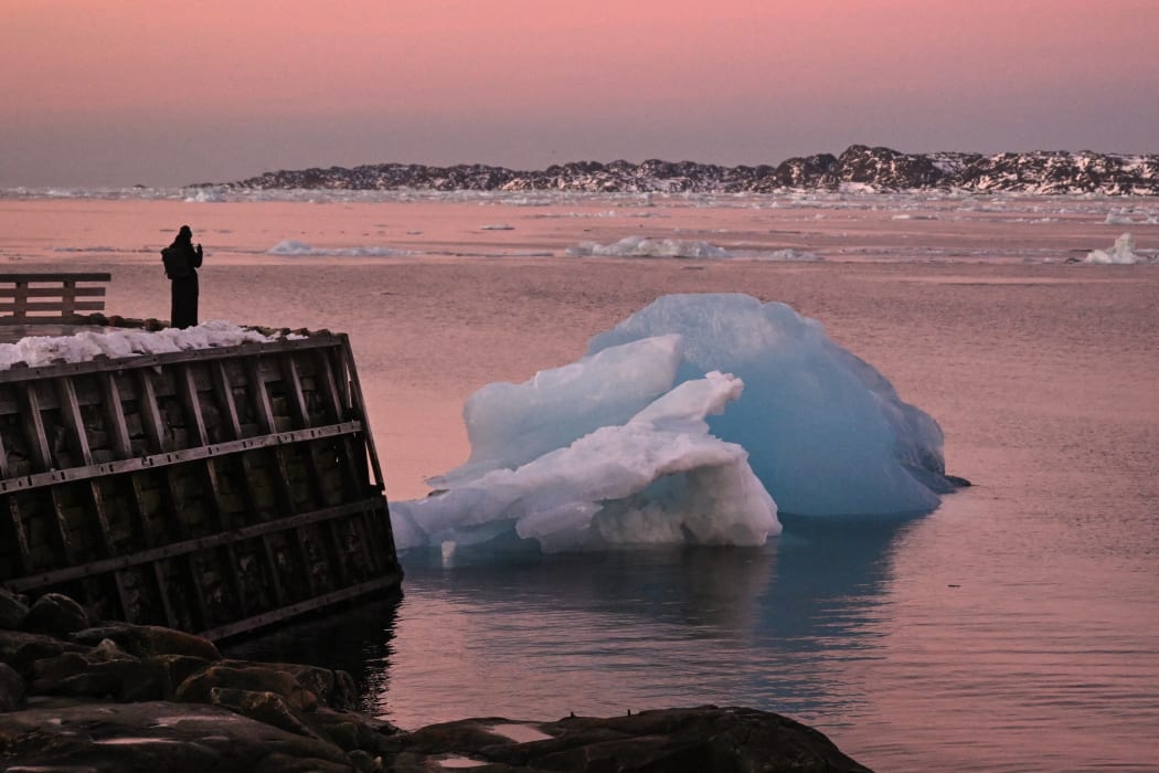 A woman takes a photo of an ice block at the harbour in Nuuk, Greenland, on January 29, 2026. (Photo by Ina FASSBENDER / AFP)