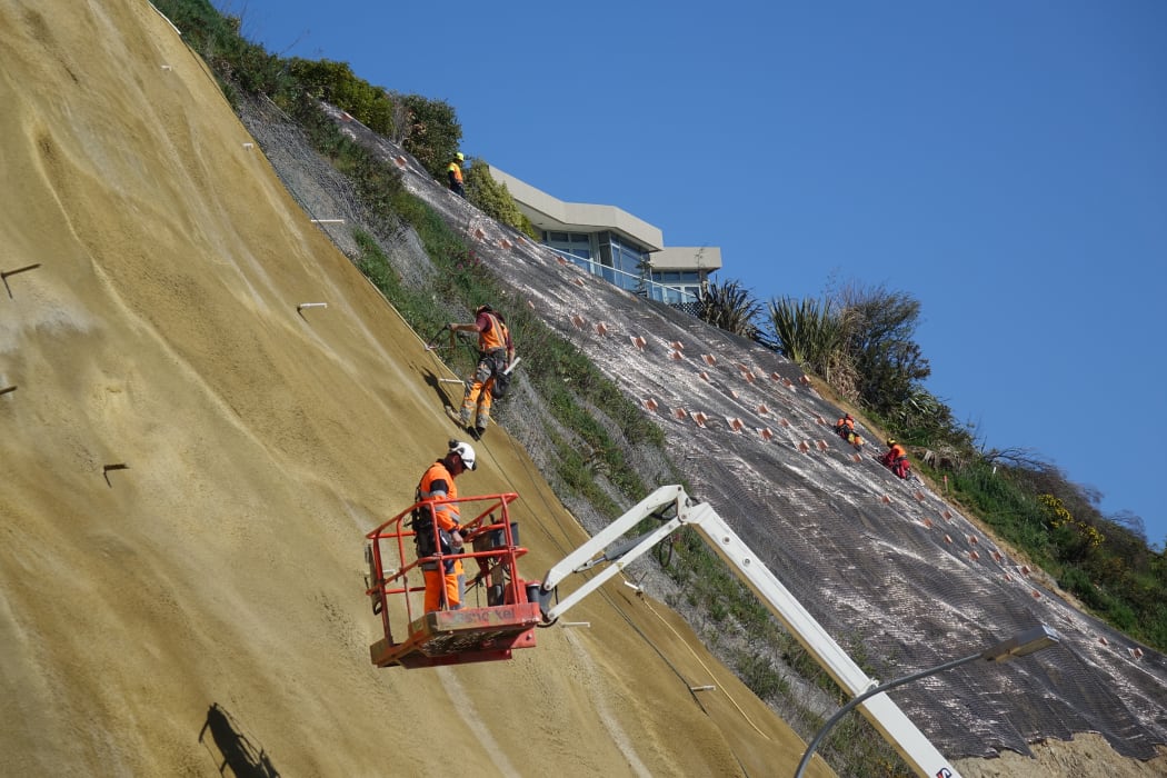 Contractors scale the near vertical slopes of the cliffs above Rocks Road.