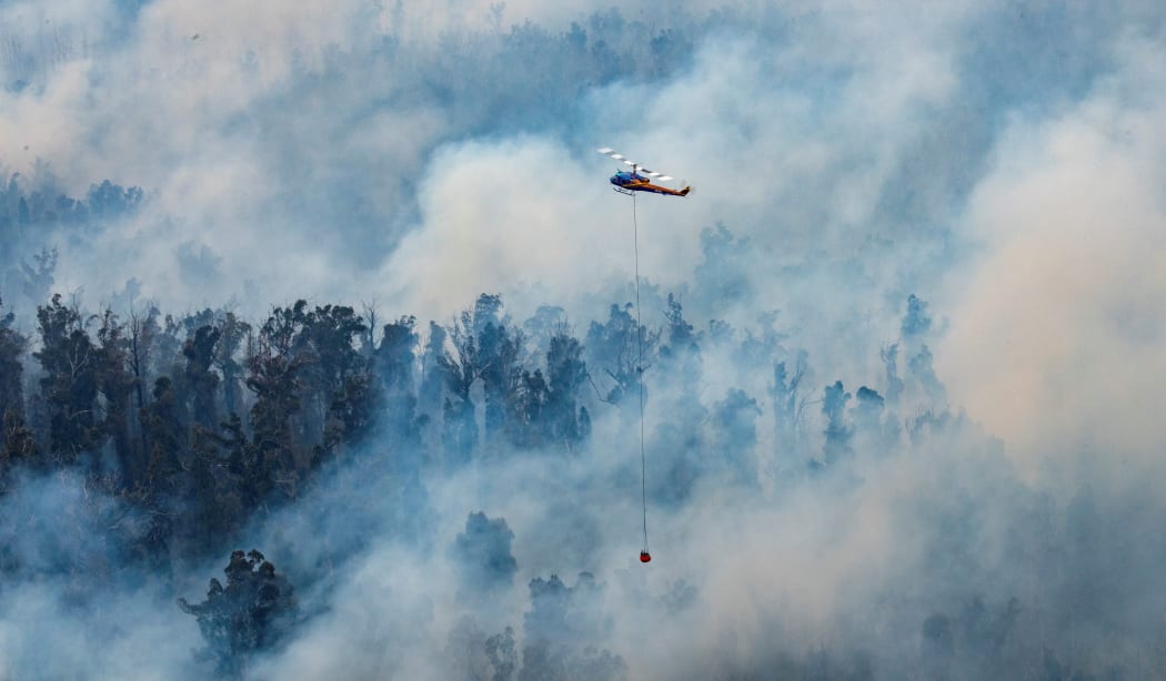 This handout photo taken on December 29, 2019 and received on December 30 from Victoria's Department of Environment, Land, Water and Planning (DELWP) shows a helicopter dumping water on a fire in Victoria's East Gippsland region.