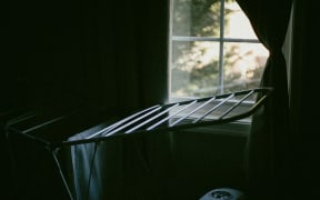 A clothes airer near a window with a little sunlight beaming through.