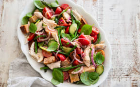 An oval serving dish containing a salad of toasted bread, basil, asparagus, red onion, tomatoes and rotisserie chicken.