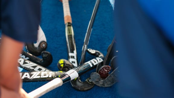 Looking down past some shoulders, we see the ends of nine hockey sticks meet against the blue field turf.