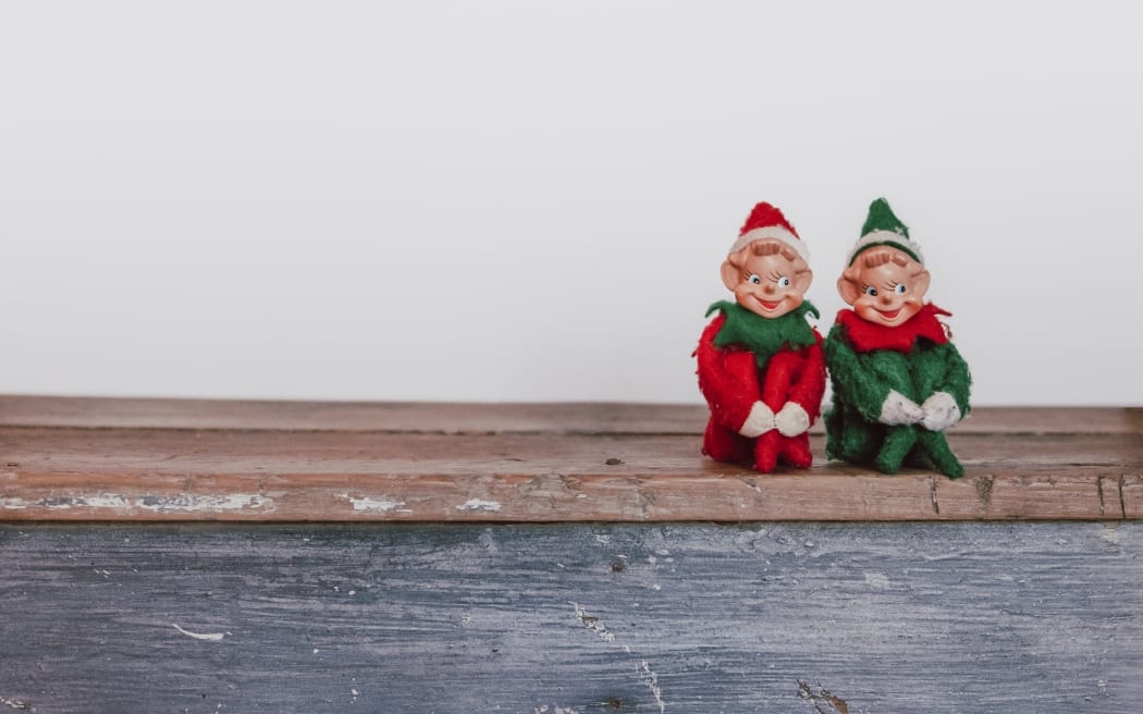 Two Christmas elves sitting on a wooden board