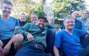 A group of men pose for a photo in a backyard. They are all smiling.