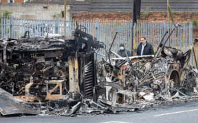 Members of the public walk past the remains of a burnt out bus on the loyalist Shankill Road in Belfast, after it was set on fire during a night of violence on April 8, 2021.