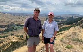 Evan and Linda Potter stand next to each other on their farm, both are wearing caps.