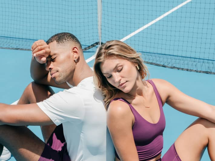 A couple in matching workoutfits sit on a tennis court.