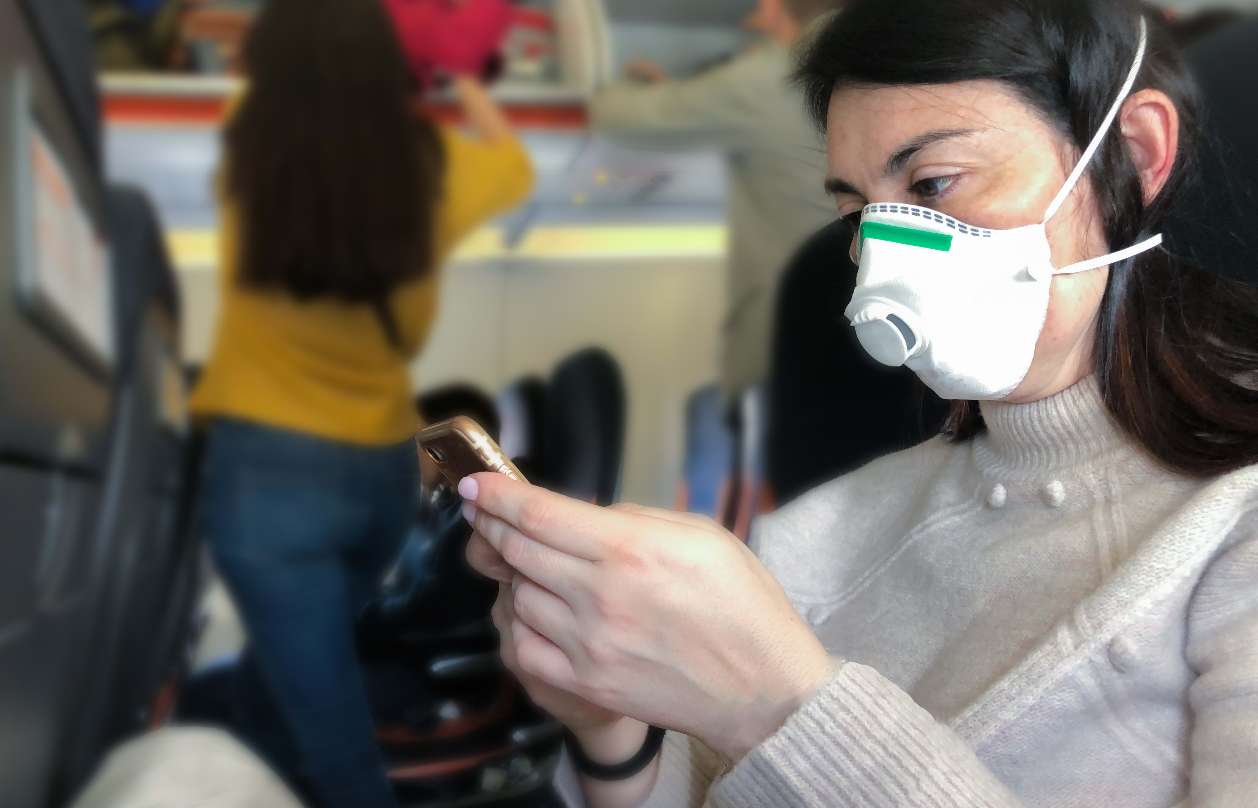 Airplane passenger with with respiratory mask looking at phone.