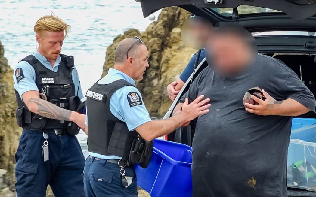 Fishery officers Korban Aitken, left, and Allan Gilmour talking to a man about the pāua in the boot of his car at Miramar in Wellington.